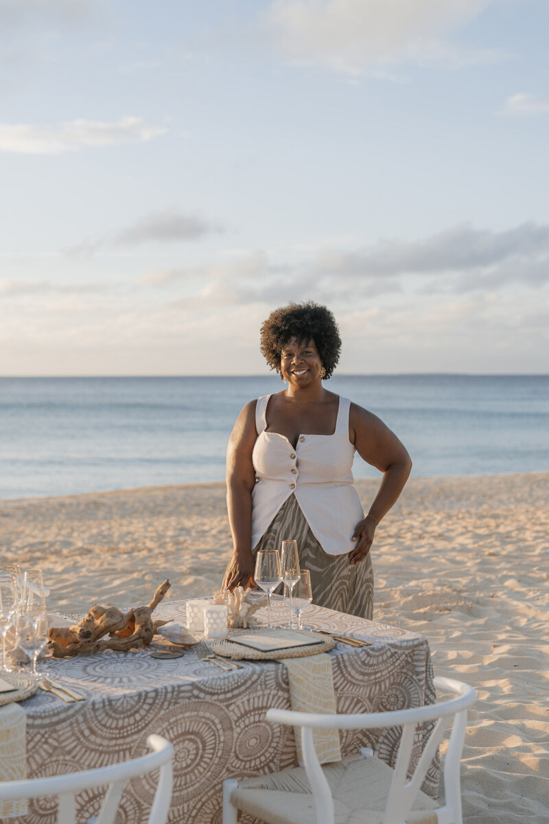 Fallon Cater - destination travel advisor – stands next to a table set up on the beach in Anguilla.