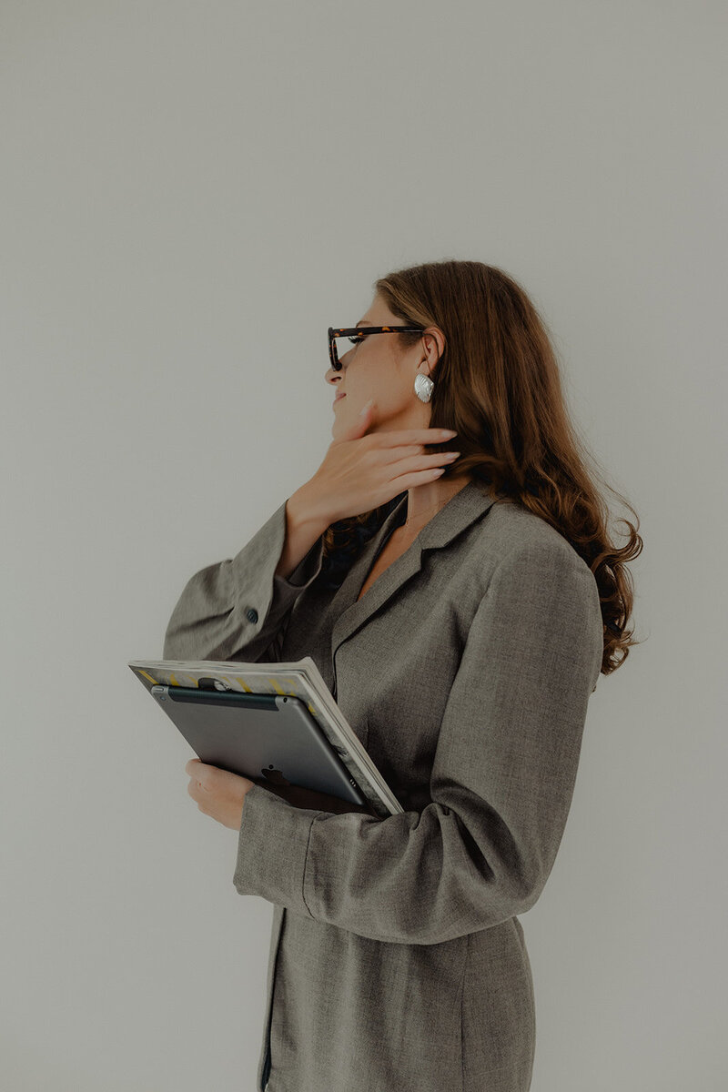 a fashionable woman in a gray blazer wearing glasses and holding her ipad.