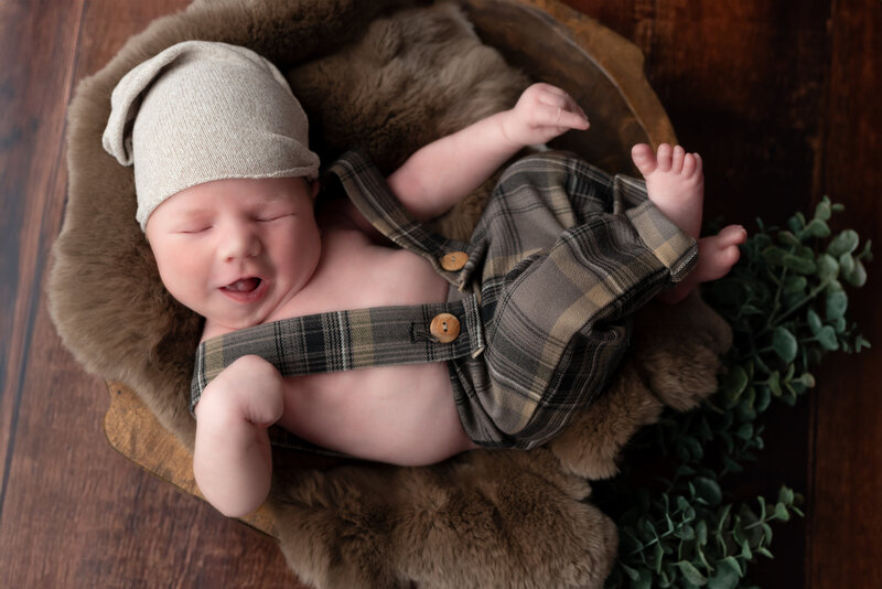 Smiling newborn in plaid overalls and soft brown textures, styled in-studio in Paris, Ontario.