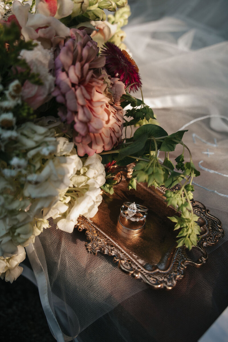 Wedding flowers and decorative elements artfully arranged with vintage lace, pearls, and textured florals on a dark surface, creating an elegant and romantic flat lay for wedding styling inspiration.