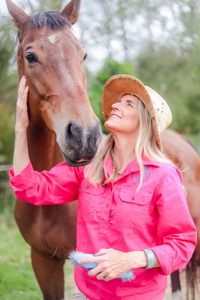 courtney brown in pink shirt and cowgirl hatlooking up at a brown horse