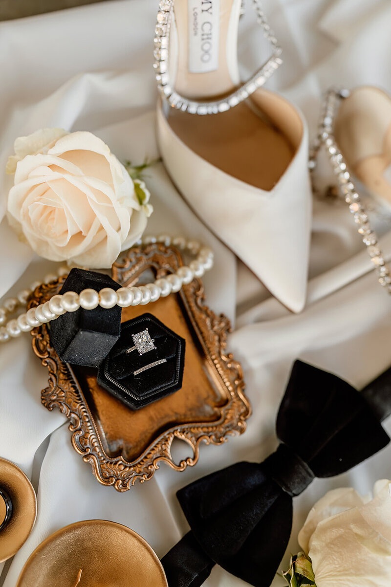 detail photo of the wedding couples rings, bow tie, shoes, and veil
