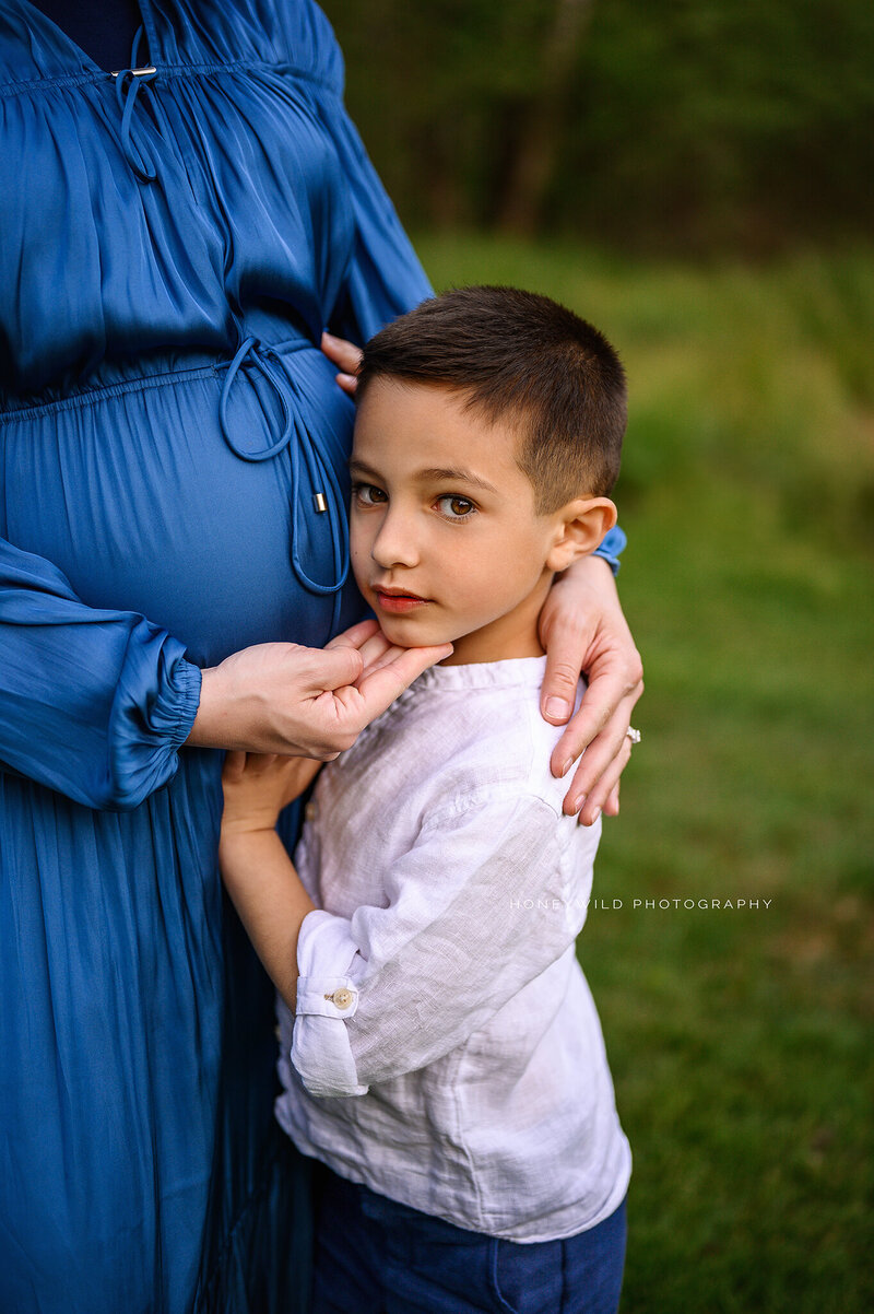 Luxury maternity session in Grand Rapids, MI—A heartfelt moment as an older sibling embraces his expecting mother, showcasing the beauty of motherhood in a timeless fine art maternity portrait by Honey Wild Photography.