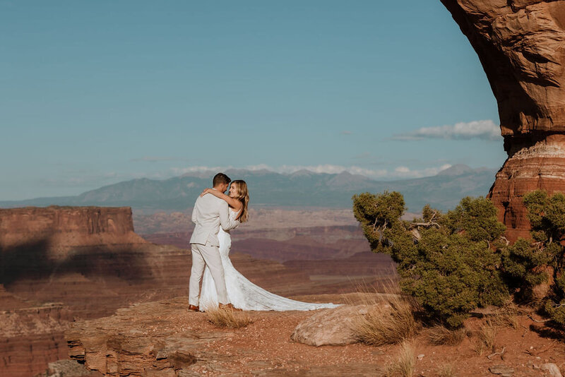 bride and groom kissing on a cliff with the desert sprawling in the background