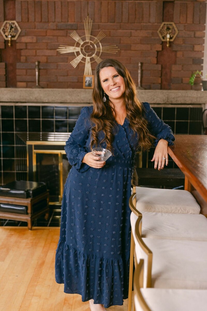 Jennifer holding a cocktail in front of a fireplace