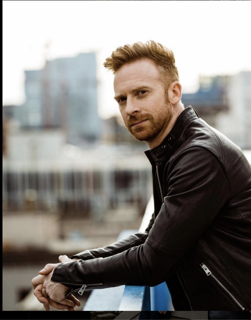 Photo of guitarist Jake Turner in black leather jacket against a city backdrop. 
