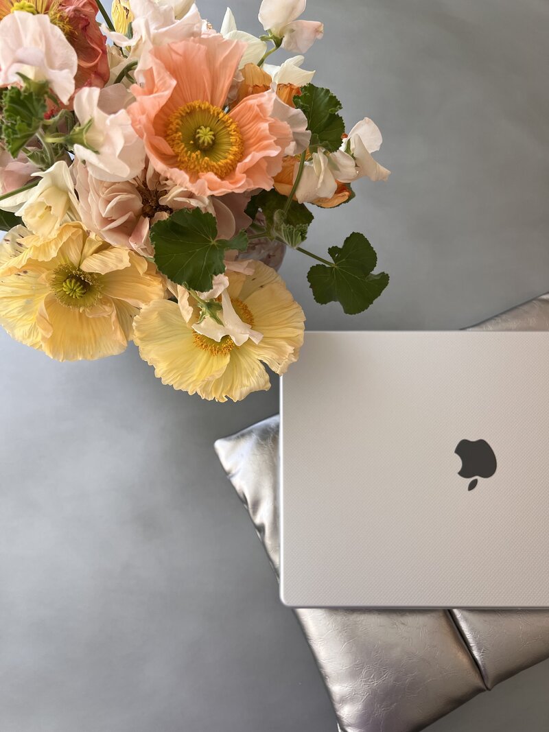 Laptop sitting on a grey surface next to a vase of colorful flowers