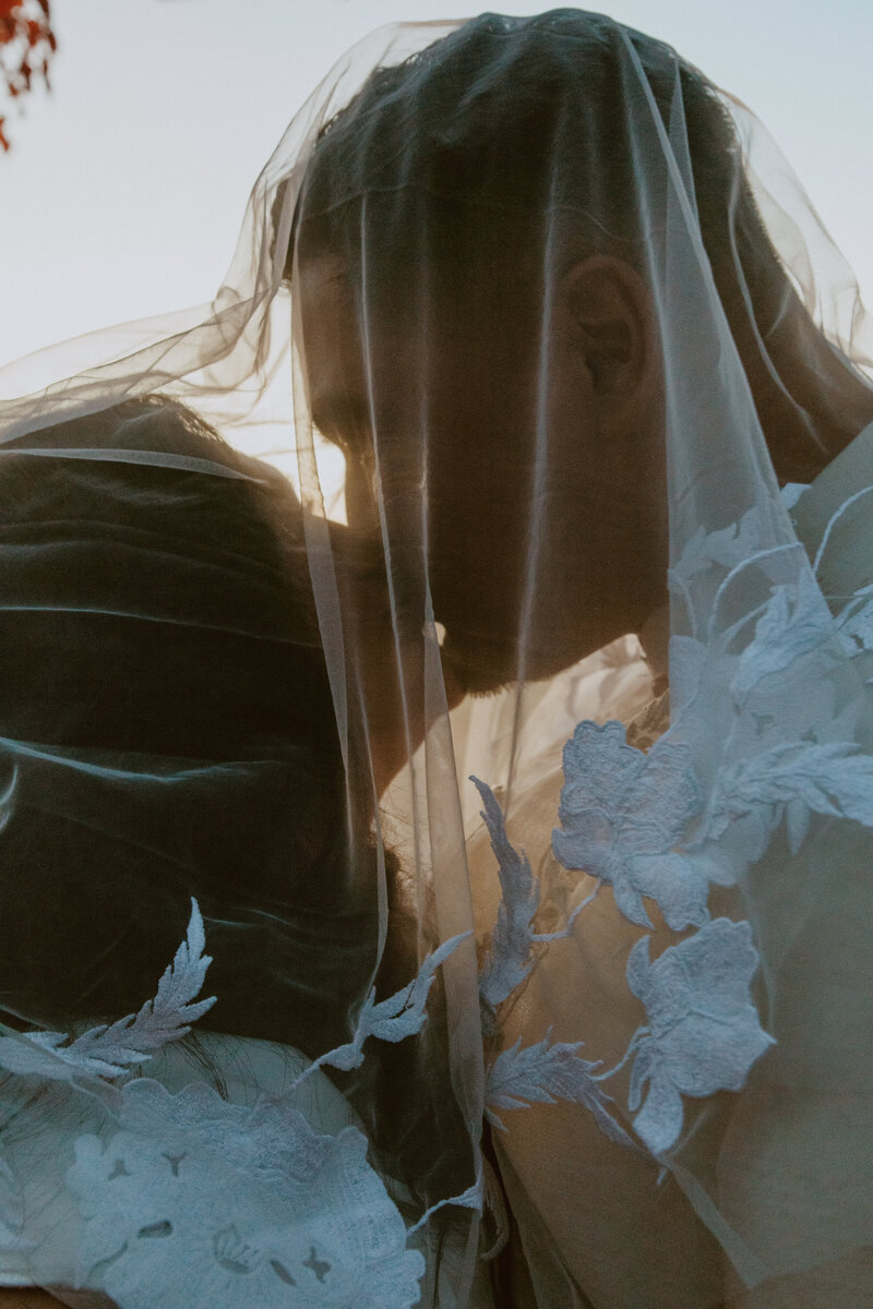 Bride and groom kissing under veil at sunset