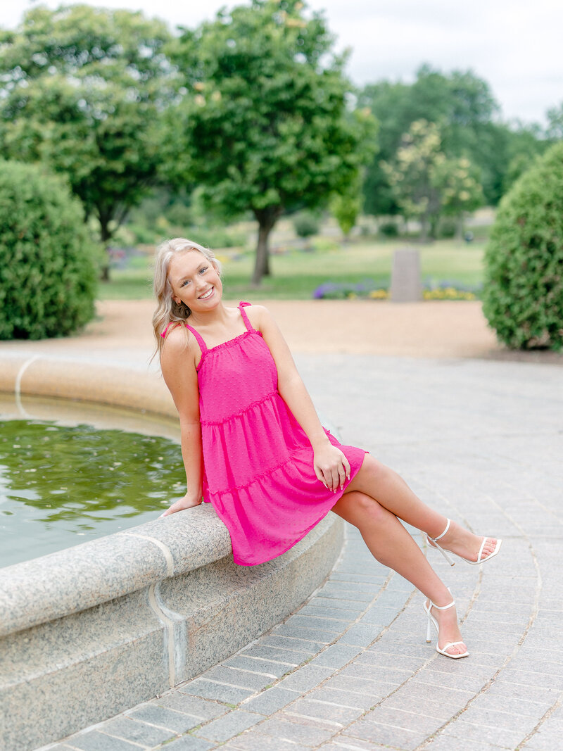 senior girl sitting on a fountain edge smiling at camera