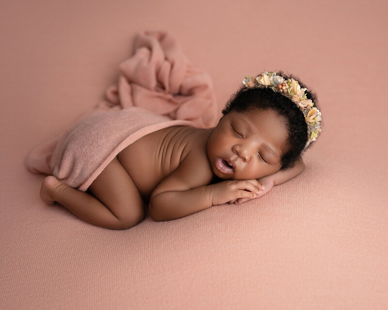 newborn girl with peach floral headband sleeping on peach blanket