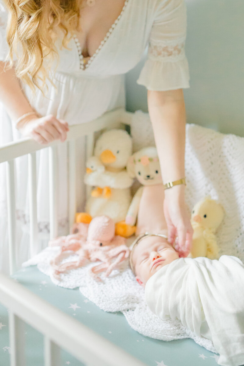 A swaddled newborn rests peacefully in a crib as the mother gently reaches over to touch her baby with love. This heartfelt moment, captured by a Westport photographer, beautifully showcases the bond between mother and child in a soft, natural setting