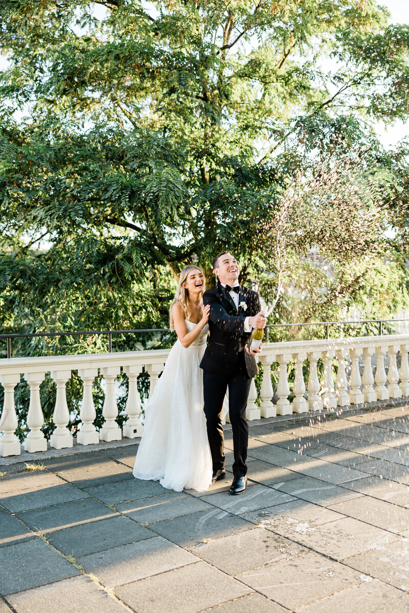 Bride and groom standing behind one another, spraying bottle of champagne