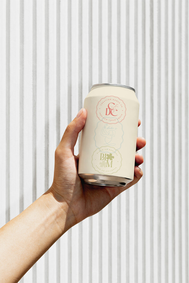 A person holds a can of soda in front of a colorful striped wall, showcasing branding for a dance studio.