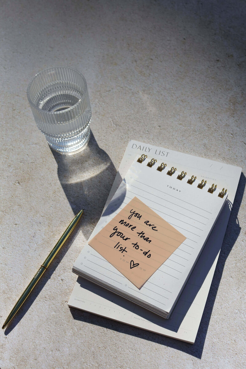 A notepad, pen, and glass of water symbolize the importance of taking breaks and prioritizing well-being over tasks.