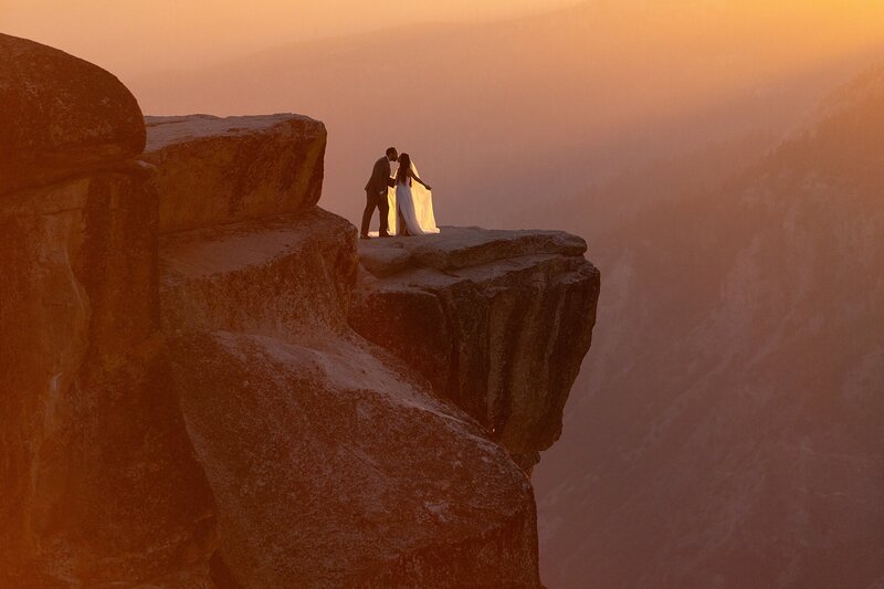 A bride and groom kiss on Taft Point during sunset.