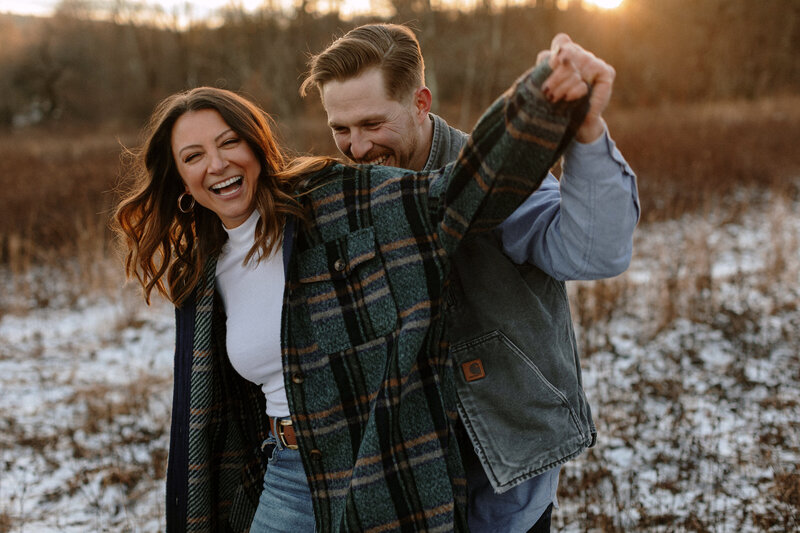 A joyful couple embraces in a snowy landscape during their winter engagement session, surrounded by a serene winter wonderland.