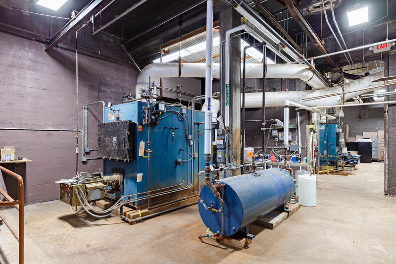 Engineering facility featuring blue industrial boilers, complex piping systems, and utility equipment in a mechanical plant room.