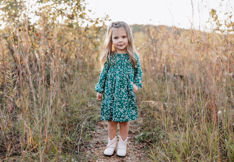 Young girl standing on a path surrounded by tall grass looking at photographer in De Soto, Missouri. 