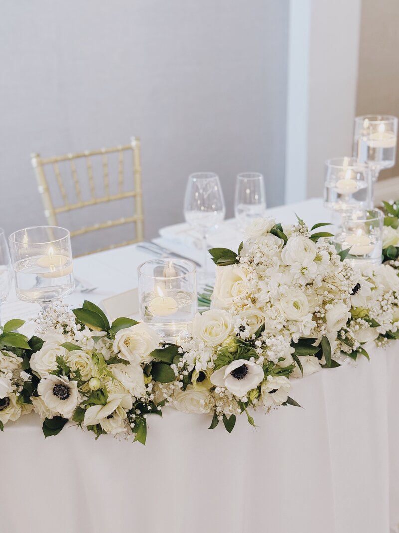 White and gold wedding reception details including all white florals and greenery and white floating candles.