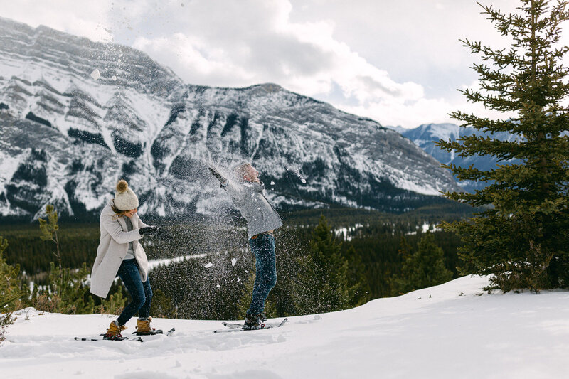 This enchanting image captures a fiancé and his partner face-to-face, embracing on the frozen expanse of Lake Louise. The majestic Victoria Glacier serves as a stunning backdrop, enhancing the intimate moment with its breathtaking scenery during their winter photo shoot.
