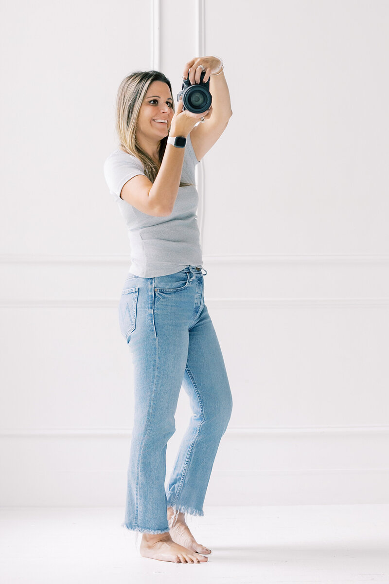 Katie Petrick standing in white outfit holding laptop, ready to help clients plan their Charlotte newborn, maternity, and family photography sessions