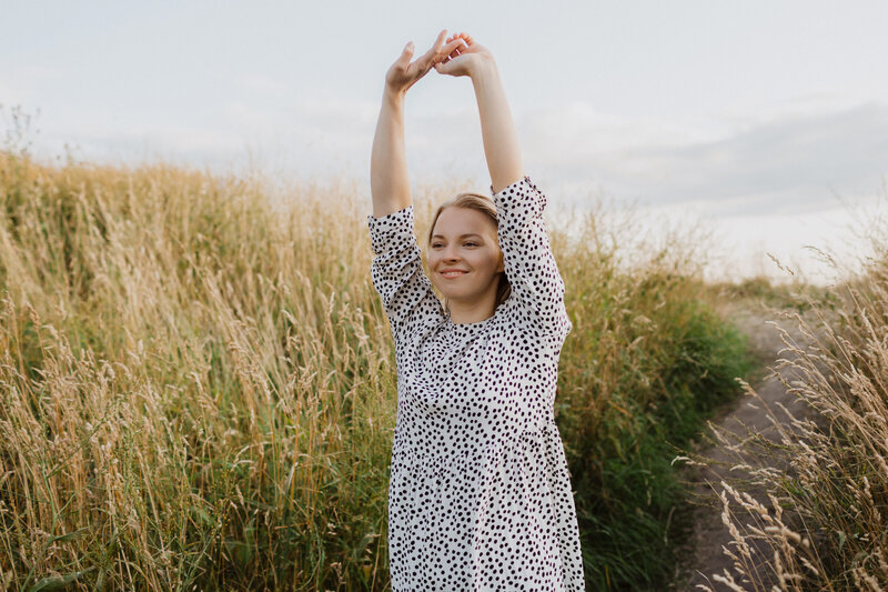Portrait of a woman holding hands up and smiling in a field of hay in Helsinki in Finland