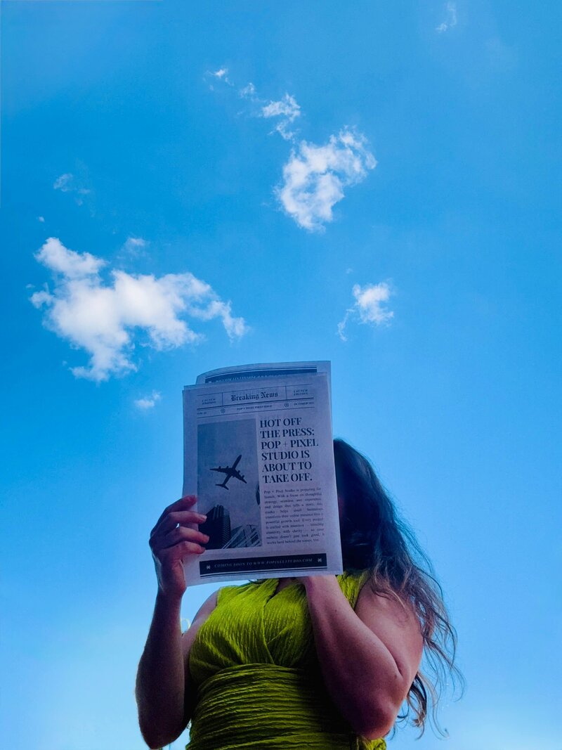 Madison, designer and founder of Pop + Pixel Studio, holding a news paper that says "Pop + Pixel Studio is About to Take Off."