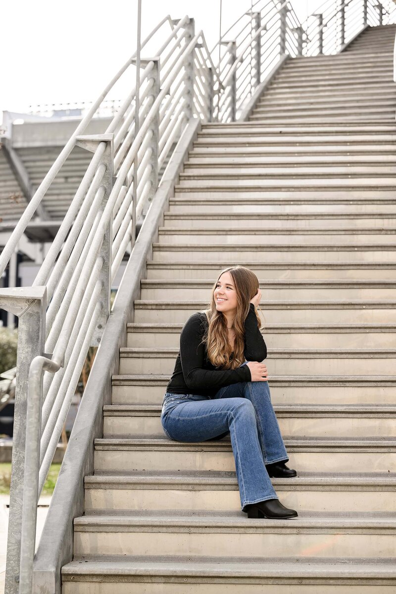 queen city stairwell is background for charlotte area grad photo session with senior sitting on stairs wearing black shirt and jeans