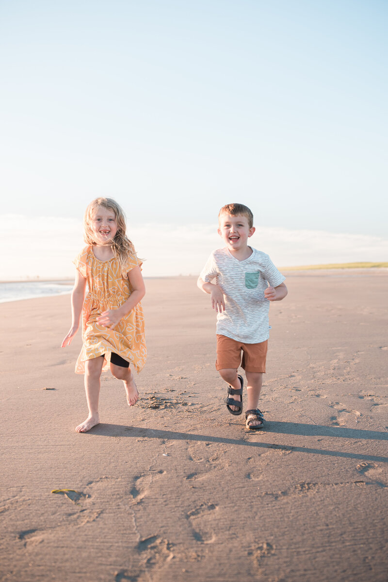 Family of 4 walking away from tall rock formations on the Oregon Coast, footprints left in the sand along the water line 