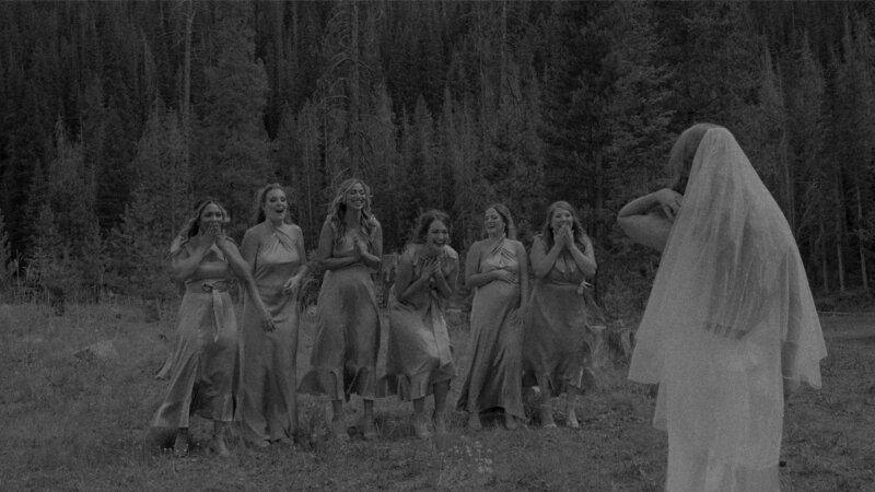 Person in wedding dress standing facing bridesmaids who are celebrating
