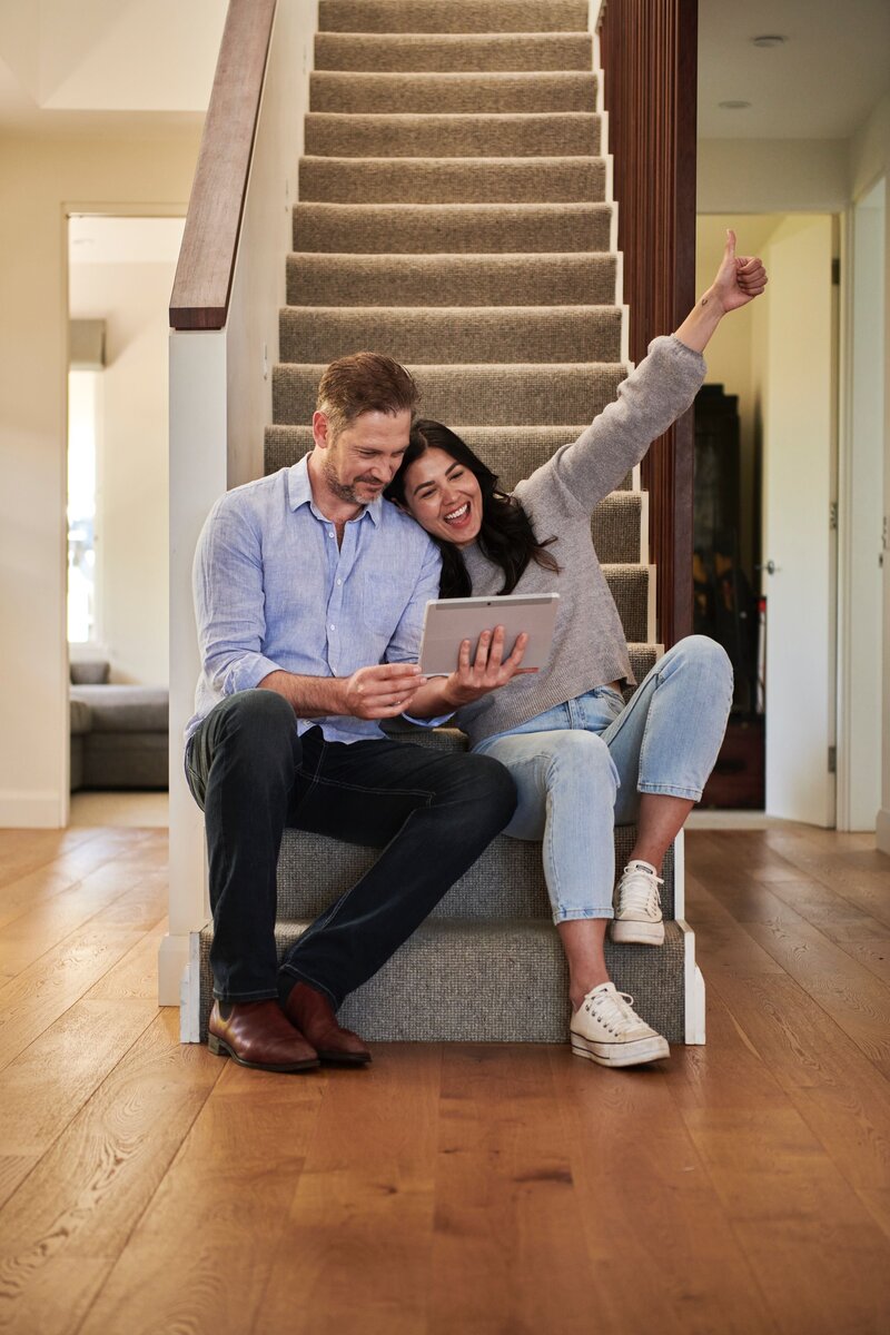 couple sitting on stairs reading tablet and looking happy