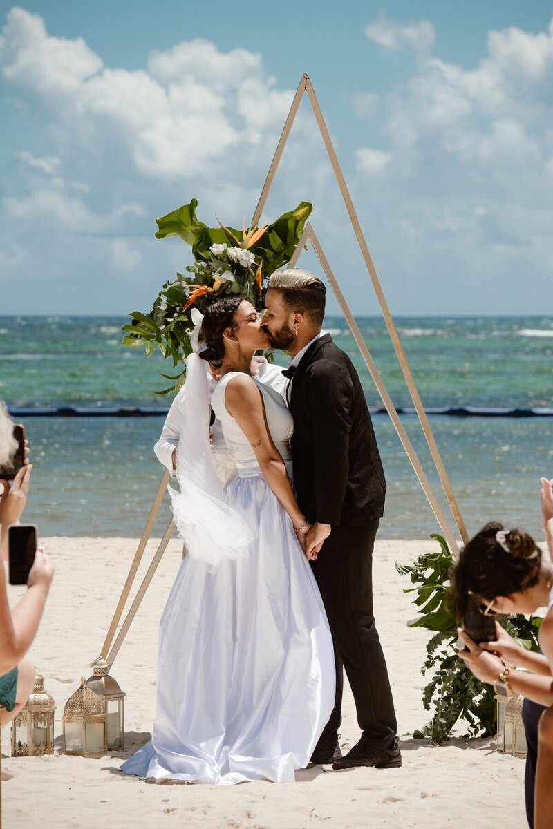 Couple kissing at their wedding ceremony on the beach planned by travel agent for destination wedding, specializing in tropical vacations