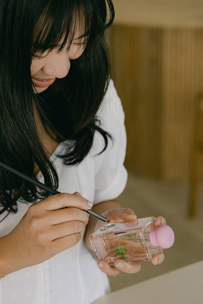 Female artist painting on glass perfume bottle.