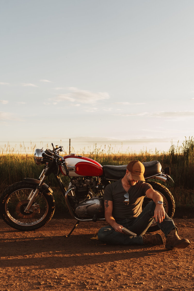 Man sitting on ground outside by his motorcycle