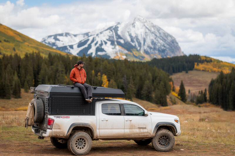A man sitting on top of a truck camper, Mt. Crested Butte in the background