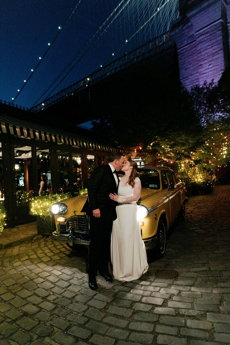 Carley and Shane at night beside a vintage taxi near the Brooklyn Bridge