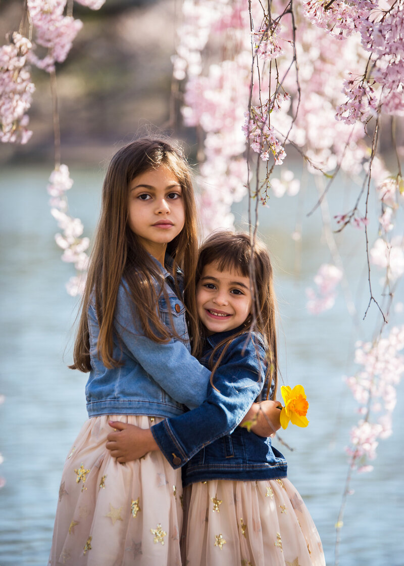 Siblings hugging in front of cherry blossoms at an Essex County, NJ park.