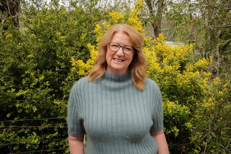 Suzanne Harrison wearing a blue turtleneck seater in front of a yellow and green tree 