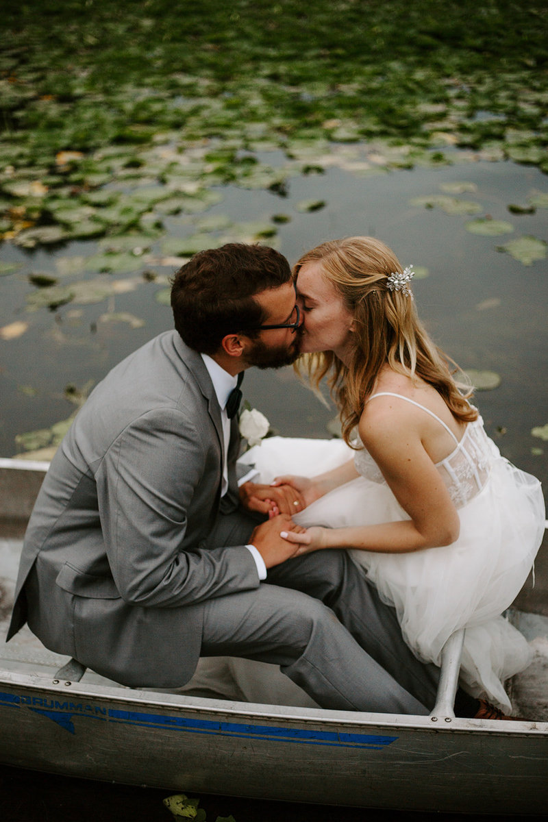 Couple kissing holding hands and sitting in a canoe on their Minneapolis Elopement day