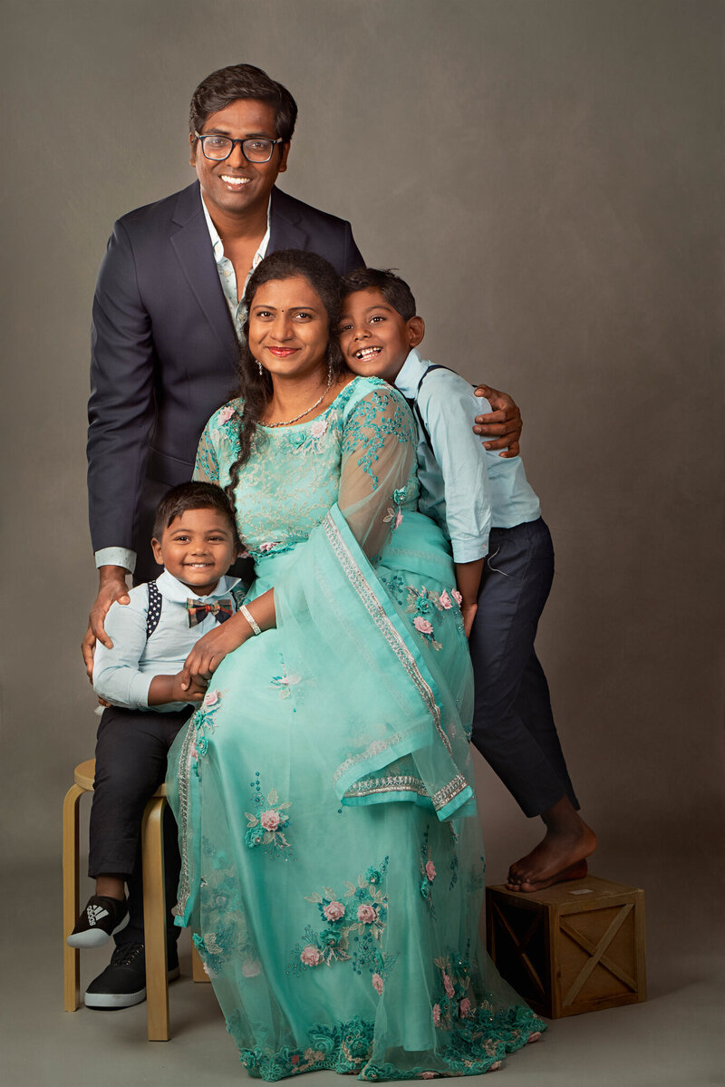 Sophisticated studio family portrait featuring parents and two young boys, with the mother wearing a stunning turquoise embroidered gown. Captured in Overland Park, Kansas, this polished setup is ideal for families seeking timeless and formal family photography in the Kansas City metro area.