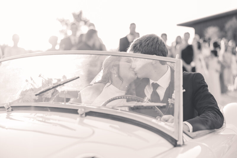 bride and groom kissing in the front of a vintage car