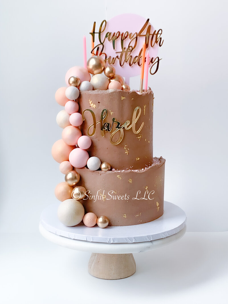 Two tier birthday cake with brown frosting, pink decorations and gold birthday and name signs.