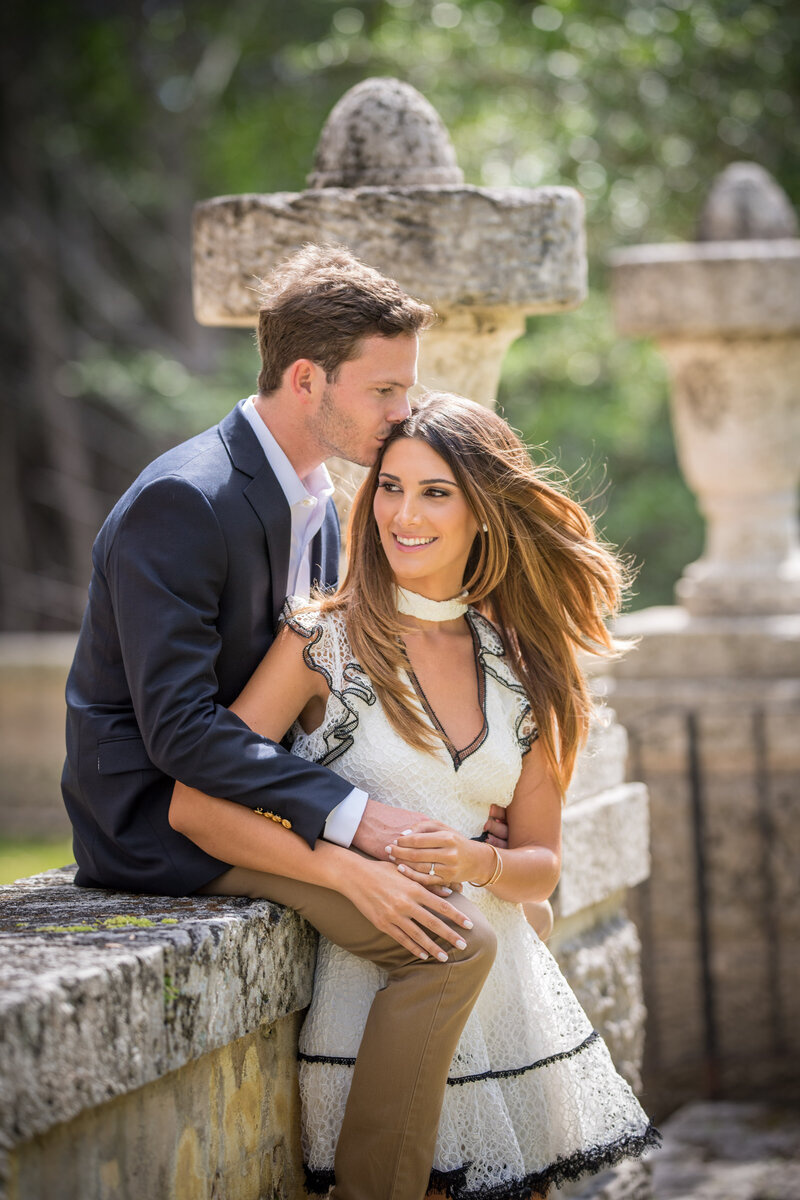 Romantic couple portrait at Vizcaya Gardens in Miami, Florida, featuring a man in a suit gently kissing his partner on the forehead, captured by Rodrigo Varela Photography.