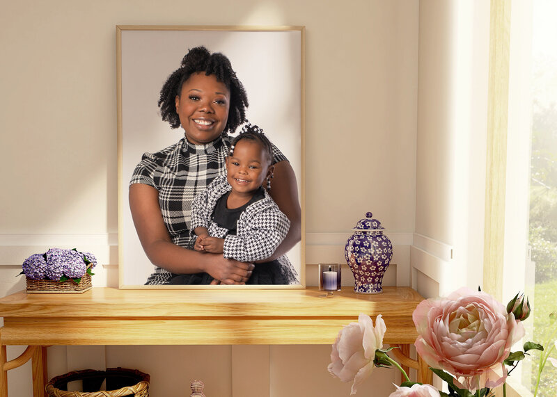 Professional portrait of a framed print  of mom and daughter sitting on a desk in a room .