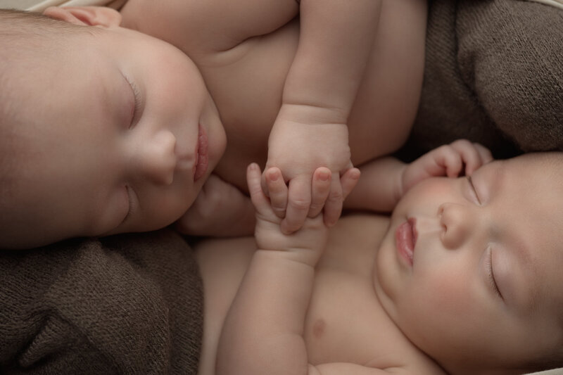 Twin newborn boys holding hands in a heartfelt, skin-to-skin pose – timeless twin portrait in Paris, Ontario.