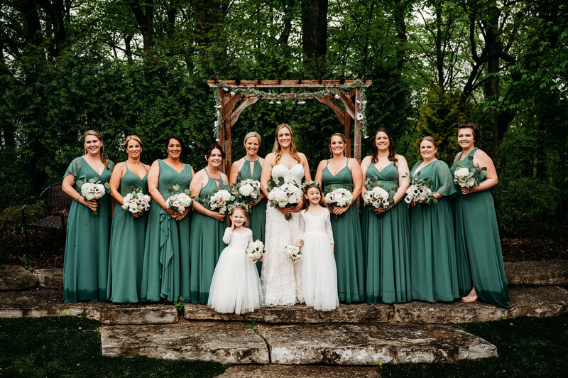 Bride and 8 bridesmaids and  2 flower girls standing in a  line and smiling