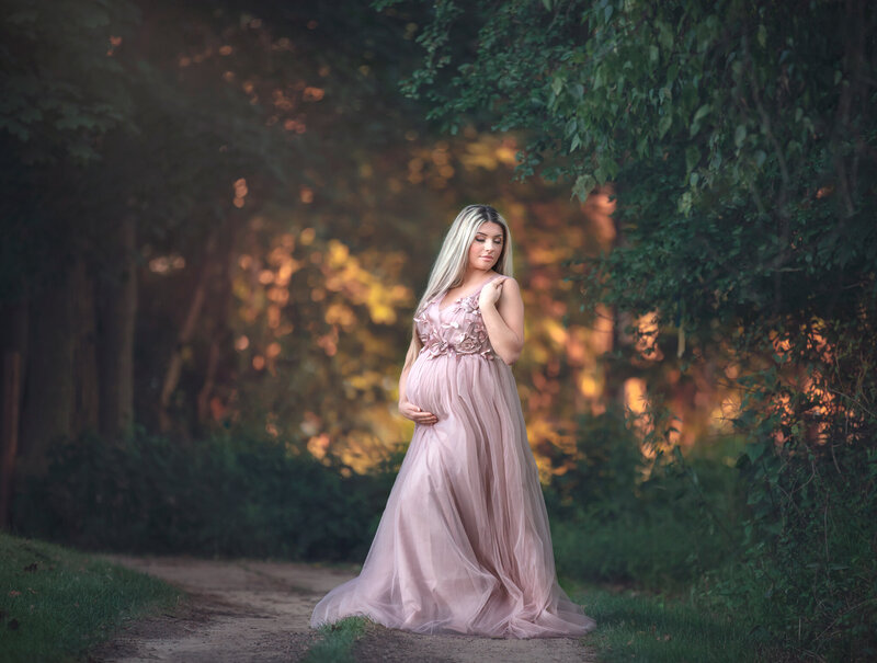 "Beautiful pregnant mom in a flowing pink gown, posing in a serene forest setting, captured in a breathtaking maternity photography session in Ottawa."