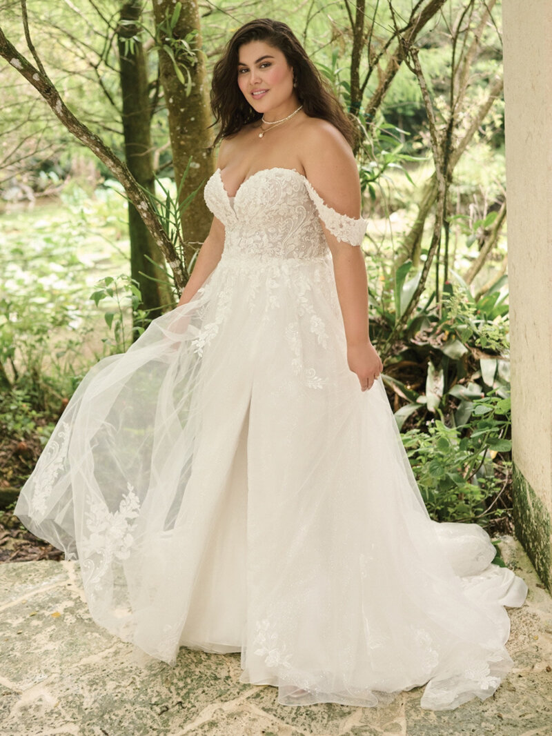 Bride wearing off shoulder wedding dress doing a post outdoors