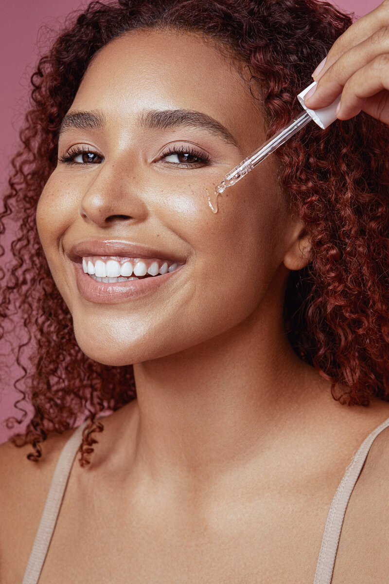 Jazz Walters smiling while applying a skincare product with a brush, showcasing a glowing complexion, photographed by Ylva Erevall.