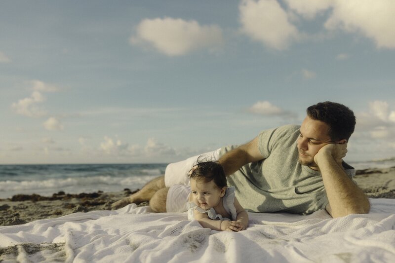 father poses with daughter for family photos on beach